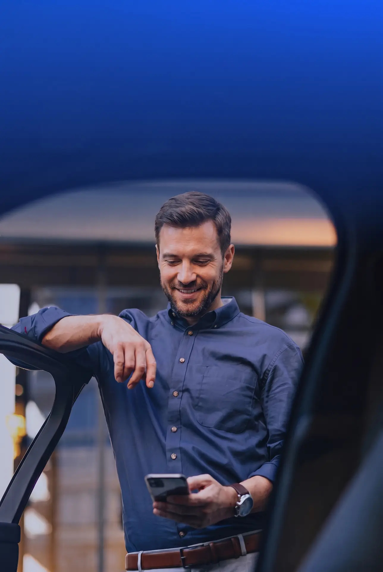 A man leaning on an open car door, checking his phone